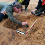 07-In enkele sporen van palen zijn munten gevonden, hier wordt door Jan-Willem de Kort een vondst blootgelegd